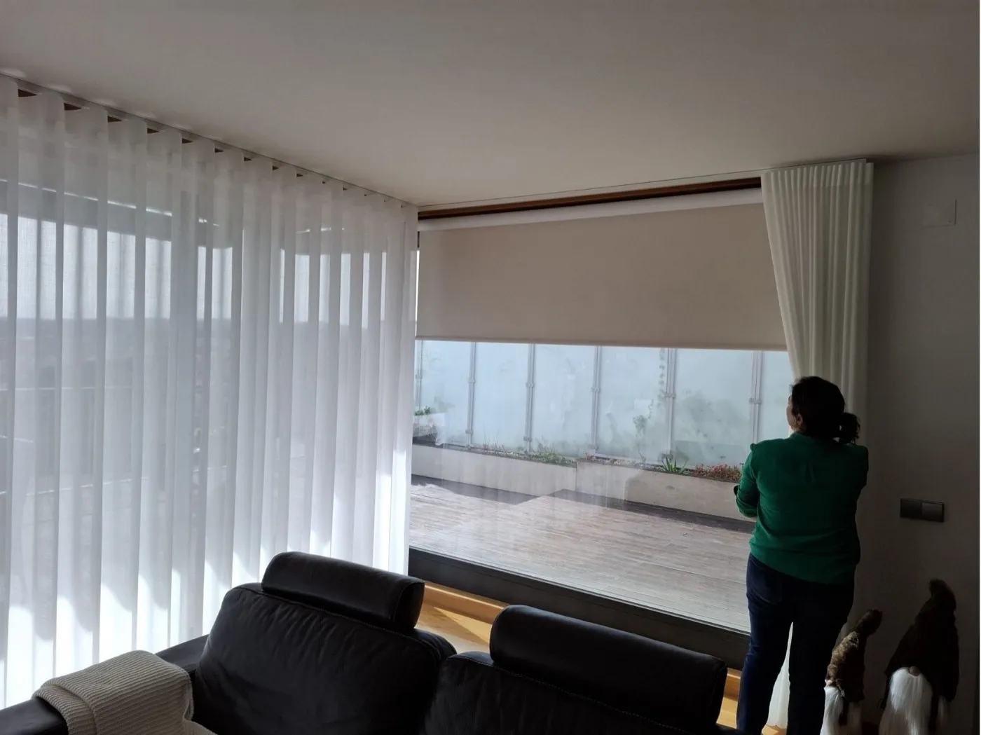 Blackout descido sobre uma janela de sala, com cortinado transparente ao lado